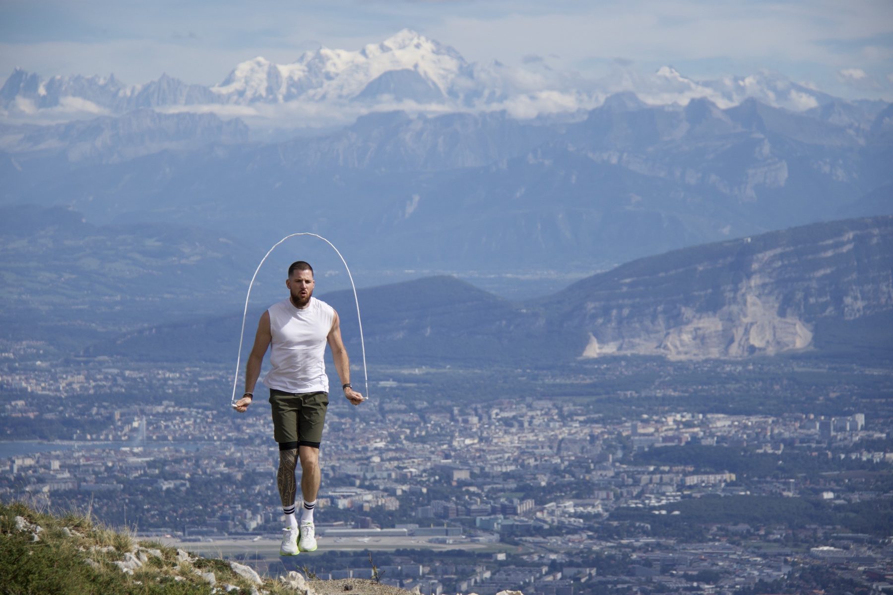 Kilian saute à la corde face aux Alpes, la corde dessine son arc au-dessus de lui