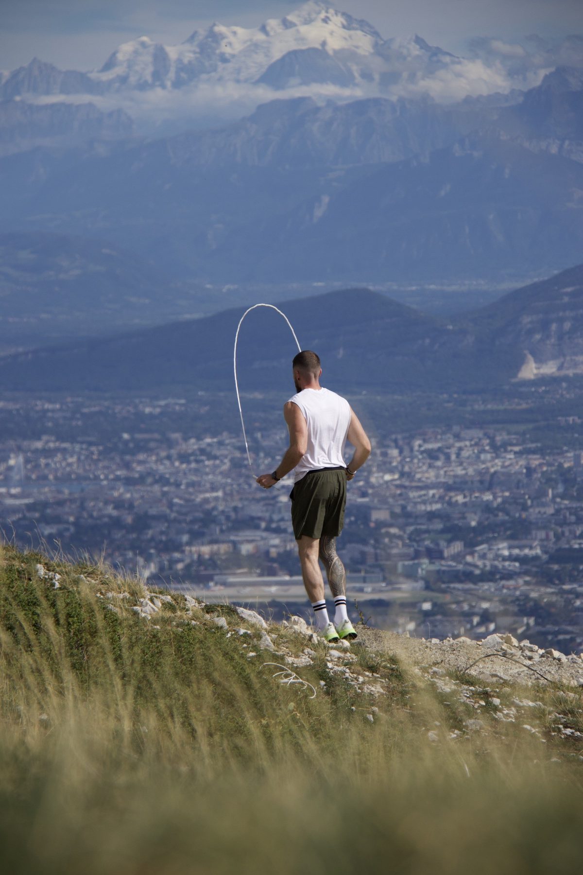 Kilian de dos, la corde dessine un arc au-dessus de sa tête, face aux Alpes